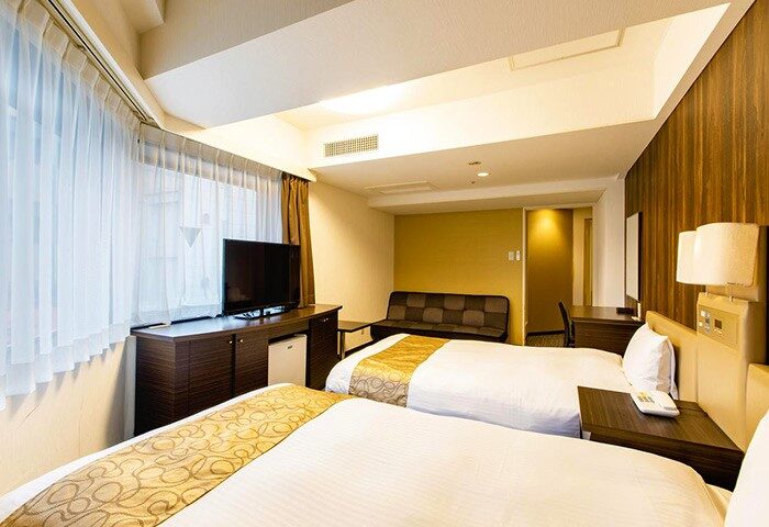 Hotel Wing International Shinjuku room. Two beds with white linens, TV, and sofa. Gay-friendly hotel in Shinjuku, Japan.