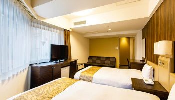 Hotel Wing International Shinjuku room. Two beds with white linens, TV, and sofa. Gay-friendly hotel in Shinjuku, Japan.