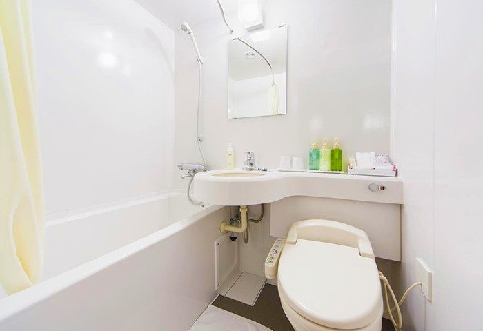 Bathroom at Hotel Wing International Shinjuku, a gay-friendly hotel. Features a bathtub, sink, mirror, and Japanese-style toilet. Clean and modern.