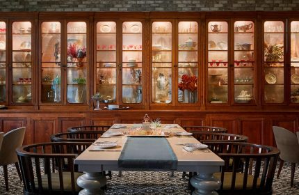 Hotel Zachary, a Tribute Portfolio Hotel, Chicago dining area. Table set in front of a large wooden cabinet filled with dishware and glassware. Gay-friendly hotel.