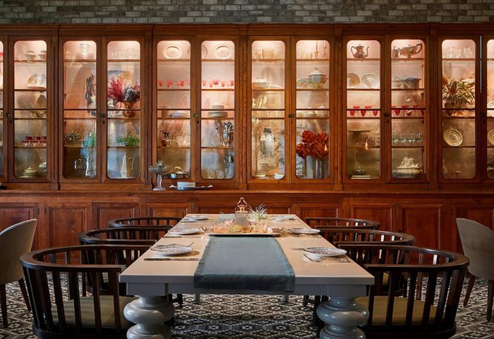 Hotel Zachary, a Tribute Portfolio Hotel, Chicago dining area. Table set in front of a large wooden cabinet filled with dishware and glassware. Gay-friendly hotel.