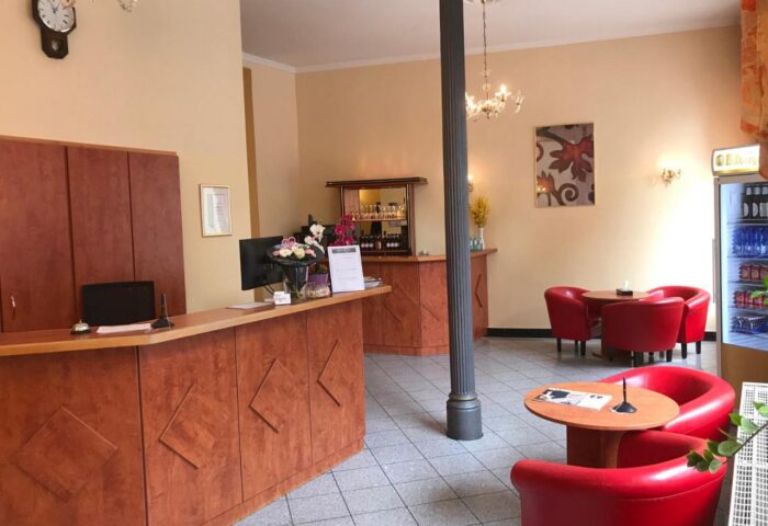 Hotel Zeil's lobby, a gay-friendly hotel. It features a reception desk, bar, and seating area with red chairs, catering to gay travelers.