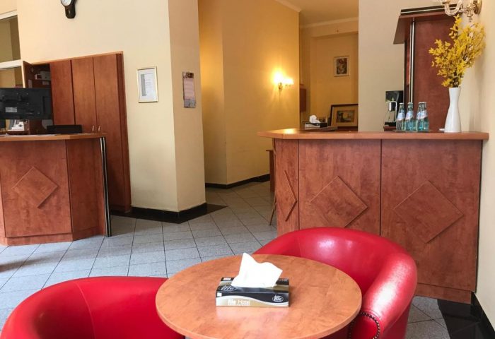 Hotel Zeil lobby interior. Gay-friendly hotel with red chairs, wooden reception desk, and warm lighting. A comfortable space for gay travelers.