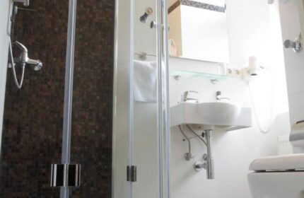 Hotel Zeil's bathroom with shower. Gay-friendly hotel room featuring modern design, white tiles, and a glass-enclosed shower. Perfect for gay travelers.