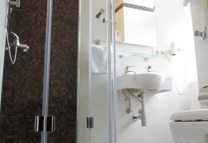 Hotel Zeil's bathroom with shower. Gay-friendly hotel room featuring modern design, white tiles, and a glass-enclosed shower. Perfect for gay travelers.