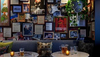 Hotel Ziggy Los Angeles's gay-friendly vibe. Wall decor with music memorabilia, Nipsey Hussle poster, and Tone-Loc flyer. Tables with drinks.