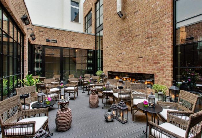 Hotel Zoo Berlin's pet-friendly, gay-friendly hotel courtyard. Wicker chairs, tables, lanterns, and a fireplace create a cozy outdoor space.