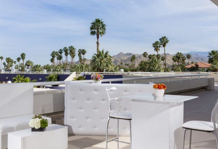 Hotel Zoso's gay-friendly rooftop bar. White modern furniture, clear chairs, and desert mountain views. Palm Springs gay travel destination.