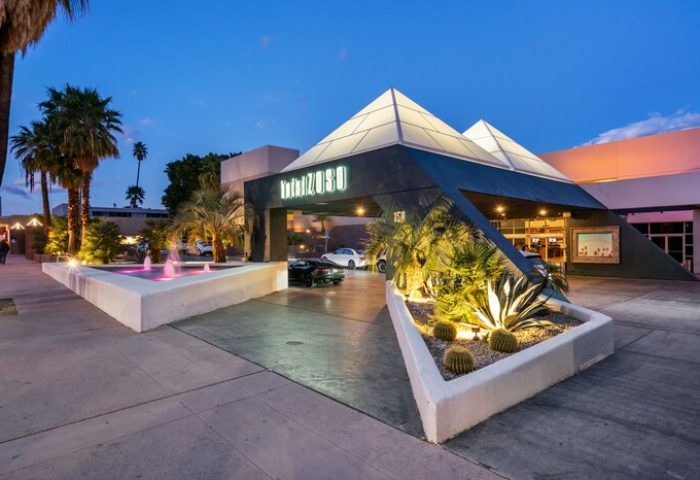 Hotel Zoso, a gay-friendly hotel. Exterior view at dusk with pyramid-shaped entrance, palm trees, fountain, and desert landscaping.