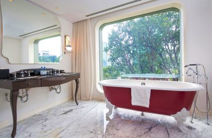 Hôtel des Arts Saigon MGallery Collection gay-friendly hotel bathroom. Red clawfoot tub by window, vanity with marble floor. Saigon travel.