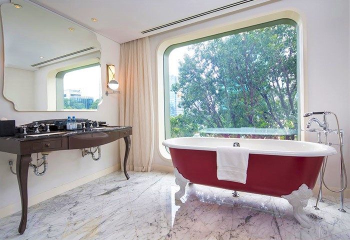 Hôtel des Arts Saigon MGallery Collection gay-friendly hotel bathroom. Red clawfoot tub by window, vanity with marble floor. Saigon travel.