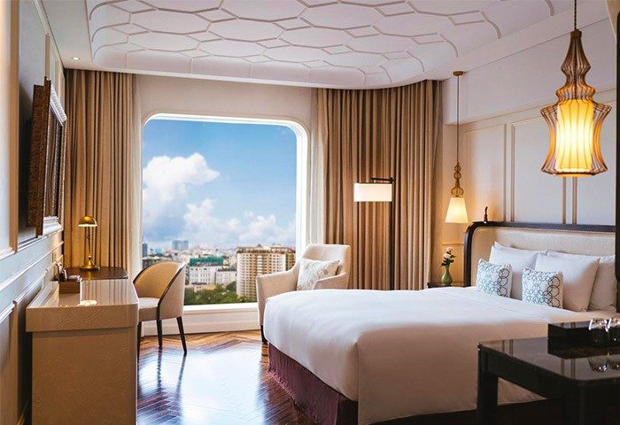 Hôtel des Arts Saigon MGallery Collection room. Gay-friendly hotel with city view, desk, chair, and bed. Saigon travel destination.