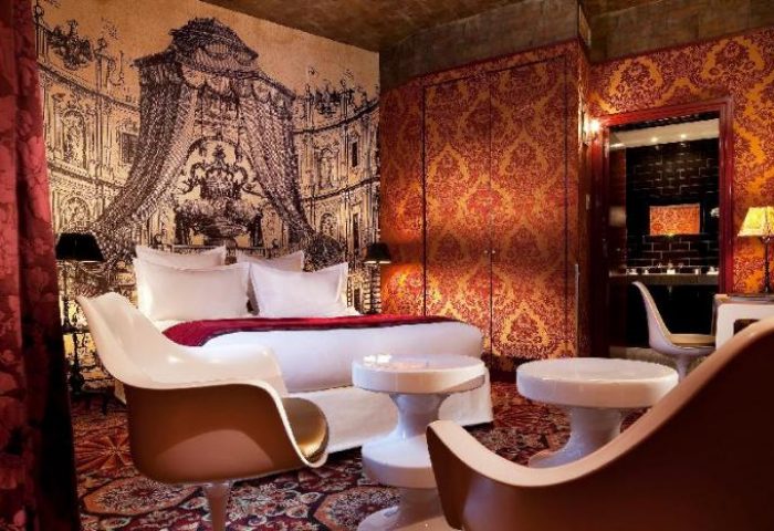 Hotel du Petit Moulin's gay-friendly room. Opulent decor with a bed, chairs, and a bathroom visible through an archway.