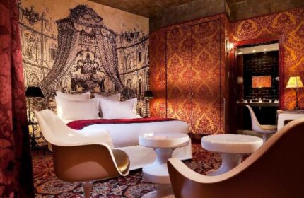Hotel du Petit Moulin's gay-friendly room. Opulent decor with a bed, chairs, and a bathroom visible through an archway.