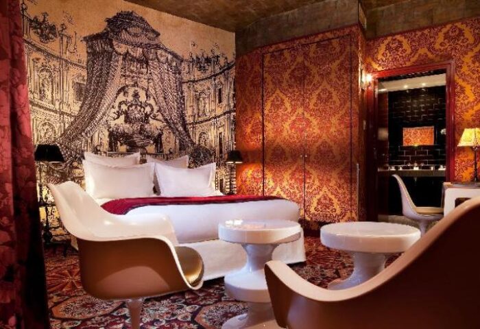 Hotel du Petit Moulin's gay-friendly room. Opulent decor with a bed, chairs, and a bathroom visible through an archway.