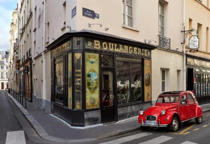 Hotel du Petit Moulin, a gay-friendly hotel: Parisian street view with a vintage red car parked in front of a classic boulangerie.