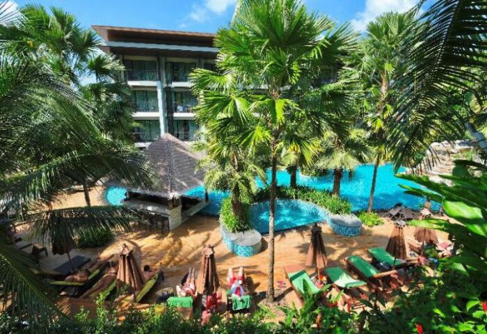 Hula Hula Resort Ao Nang, a gay-friendly hotel. View of the pool area with palm trees, sun loungers, and a bar. A tropical paradise.