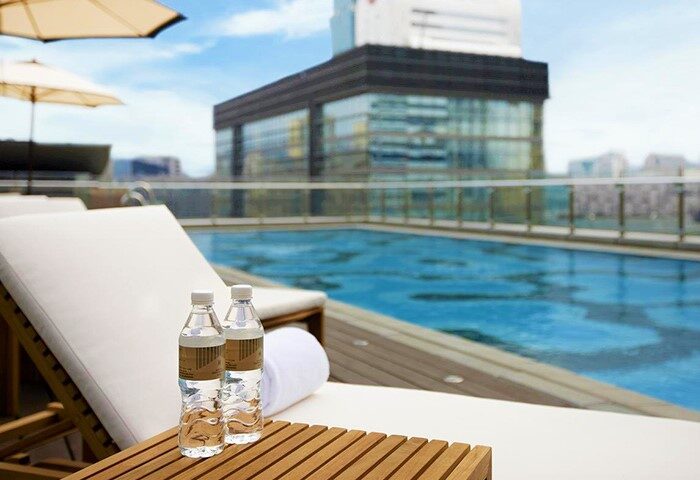 Poolside view at Humble House Taipei, a gay-friendly hotel. Lounge chairs, water bottles, and a blue swimming pool offer a relaxing experience.