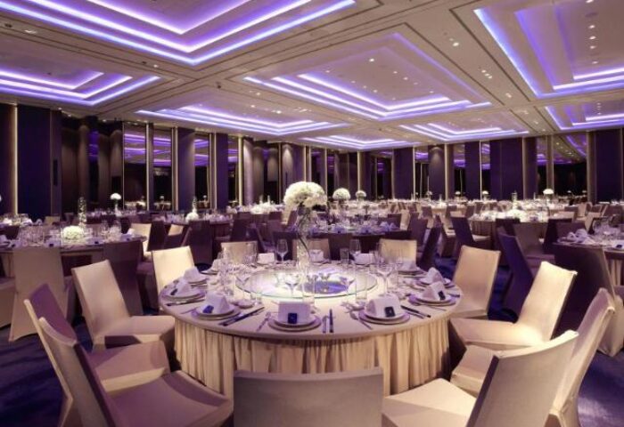 Humble House Taipei ballroom. Round tables with white linens and chairs fill the room. Purple lighting adds to the elegant ambiance. Gay-friendly hotel.