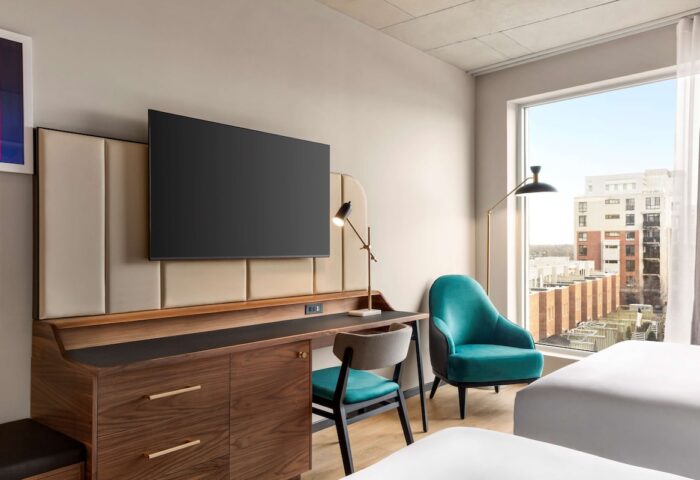 Hyatt Centric Montreal guest room. Modern gay-friendly hotel room with desk, TV, turquoise chair, and city view. Perfect for gay travel.