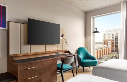Hyatt Centric Montreal guest room. Modern gay-friendly hotel room with desk, TV, turquoise chair, and city view. Perfect for gay travel.
