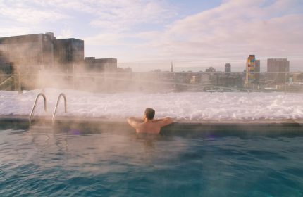 Gay-friendly Hyatt Centric Montreal: Man relaxing in rooftop pool, snow-covered edge, city skyline view. Ideal for gay travel, Montreal.