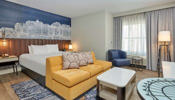 Hyatt Centric The Pike Long Beach gay-friendly hotel room. Bed, yellow couch, and Long Beach skyline mural. Modern design, comfortable stay.
