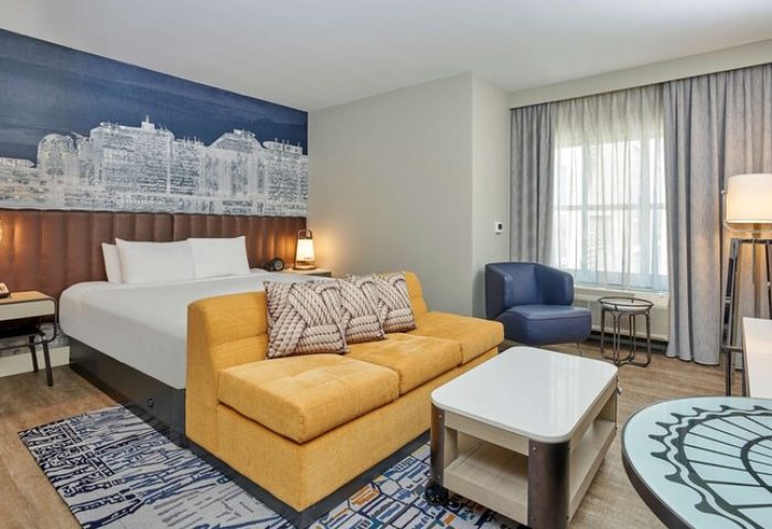 Hyatt Centric The Pike Long Beach gay-friendly hotel room. Bed, yellow couch, and Long Beach skyline mural. Modern design, comfortable stay.