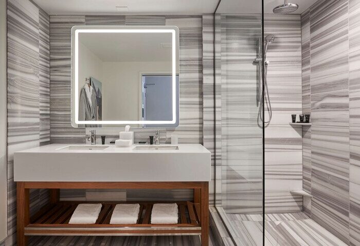 Hyatt Centric The Pike Long Beach gay-friendly hotel bathroom. Modern design with marble, glass shower, and illuminated mirror.