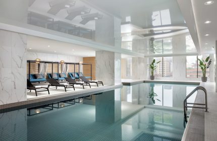 Indoor pool at the gay-friendly Hyatt Place Montreal Downtown hotel. Loungers, plants, and city views create a relaxing atmosphere.