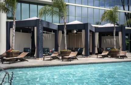 Hyatt Regency Long Beach pool with cabanas. Gay-friendly hotel with lounge chairs, palm trees, and modern design. Relaxing vacation spot.