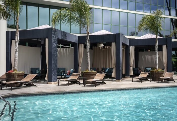 Hyatt Regency Long Beach pool with cabanas. Gay-friendly hotel with lounge chairs, palm trees, and modern design. Relaxing vacation spot.