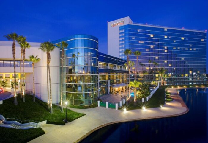 Hyatt Regency Long Beach, a gay-friendly hotel. Exterior view at dusk, featuring modern architecture, palm trees, and a reflecting pool.
