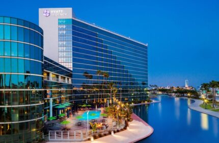 Hyatt Regency Long Beach, a gay-friendly hotel. Exterior view of the hotel with a pool, palm trees, and waterfront at dusk.