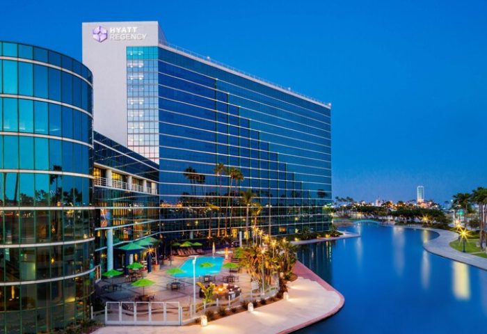 Hyatt Regency Long Beach, a gay-friendly hotel. Exterior view of the hotel with a pool, palm trees, and waterfront at dusk.