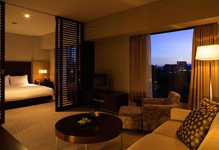 Hyatt Regency Tokyo gay-friendly hotel room. Bedroom view with a king bed, living area with sofa, chair, and a view of Tokyo at dusk.