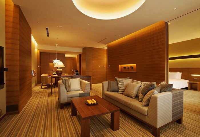 Gay-Friendly Hyatt Regency Tokyo hotel suite. Living area with sofa, chair, coffee table, and bedroom in background. Luxury gay travel.