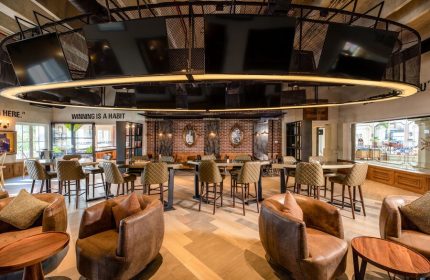 Hyatt Zilara Cancun's stylish bar area. This gay-friendly hotel features brown leather chairs, high-top tables, and a unique overhead TV display.