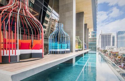 I'M Hotel gay-friendly hotel pool view. Colorful birdcage-like cabanas with pillows line the infinity pool edge, city view in background.