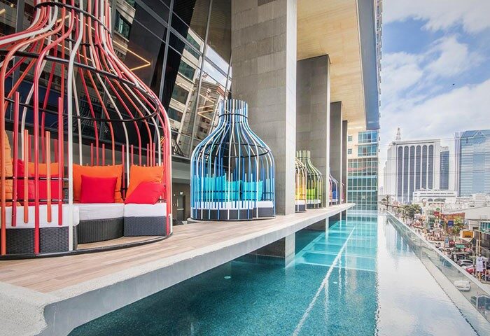I'M Hotel gay-friendly hotel pool view. Colorful birdcage-like cabanas with pillows line the infinity pool edge, city view in background.