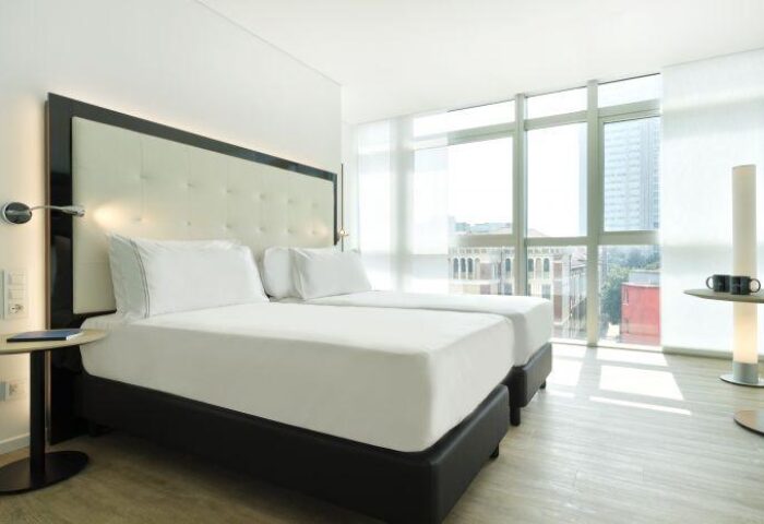 INNSiDE Milano Torre Galfa gay-friendly hotel room. Two twin beds with white linens, large window with city view. Modern, bright, and clean design.