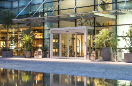INNSiDE Milano Torre Galfa entrance. Gay-friendly hotel with modern design, glass facade, plants, and decorative lanterns. Upscale Milan lodging.