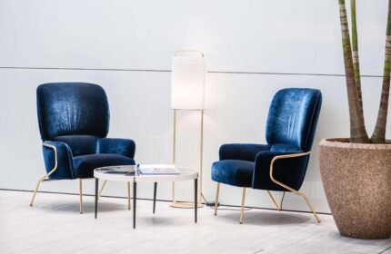 INNSiDE Milano Torre Galfa: Hotel lounge area with two blue velvet chairs, a table, and a lamp. Gay-friendly hotel interior design.