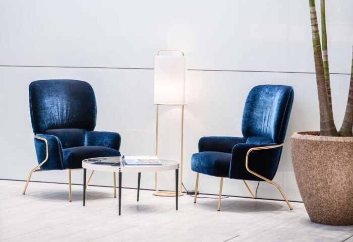 INNSiDE Milano Torre Galfa: Hotel lounge area with two blue velvet chairs, a table, and a lamp. Gay-friendly hotel interior design.