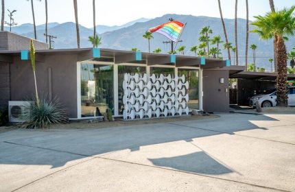INNdulge Iconic Gay Men's Resort: Gay-friendly hotel exterior with rainbow flag, mid-century modern design, palm trees, and mountain backdrop.