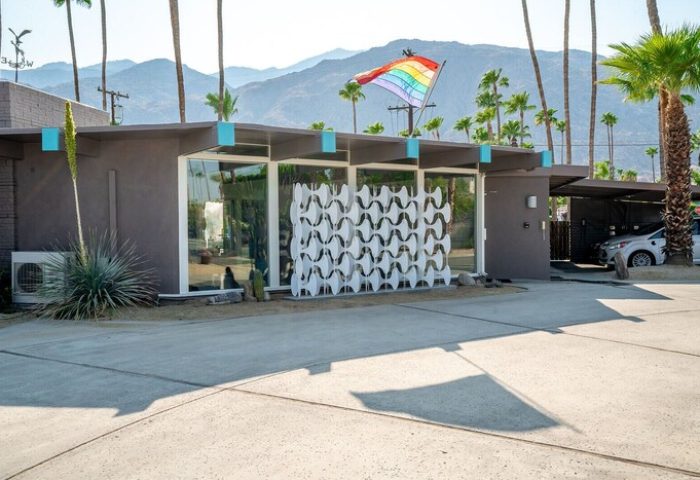 INNdulge Iconic Gay Men's Resort: Gay-friendly hotel exterior with rainbow flag, mid-century modern design, palm trees, and mountain backdrop.