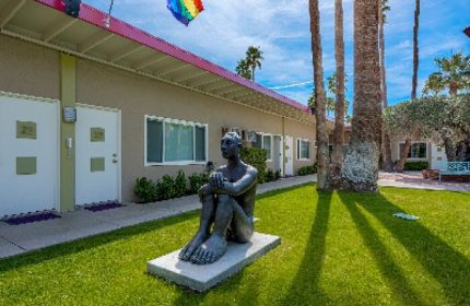 INNdulge Iconic Gay Men's Resort courtyard view. Statue, rainbow flag, and palm trees. Gay-friendly hotel for men in Palm Springs.
