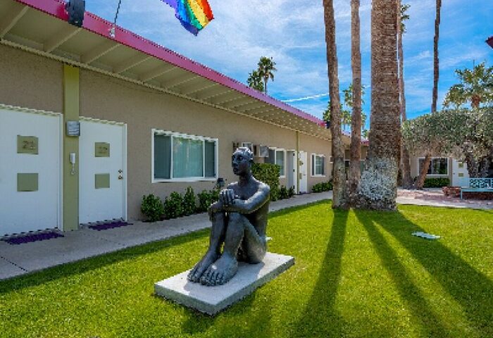 INNdulge Iconic Gay Men's Resort courtyard view. Statue, rainbow flag, and palm trees. Gay-friendly hotel for men in Palm Springs.