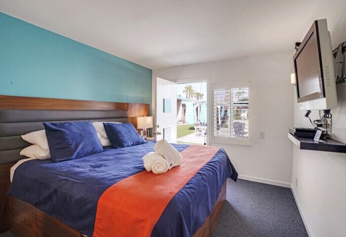 INNdulge Iconic Gay Men's Resort room. Blue bedding, orange runner, and TV. Door to patio. Gay-friendly hotel for gay men travelers.