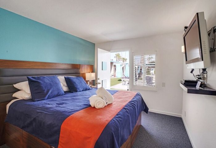INNdulge Iconic Gay Men's Resort room. Blue bedding, orange runner, and TV. Door to patio. Gay-friendly hotel for gay men travelers.